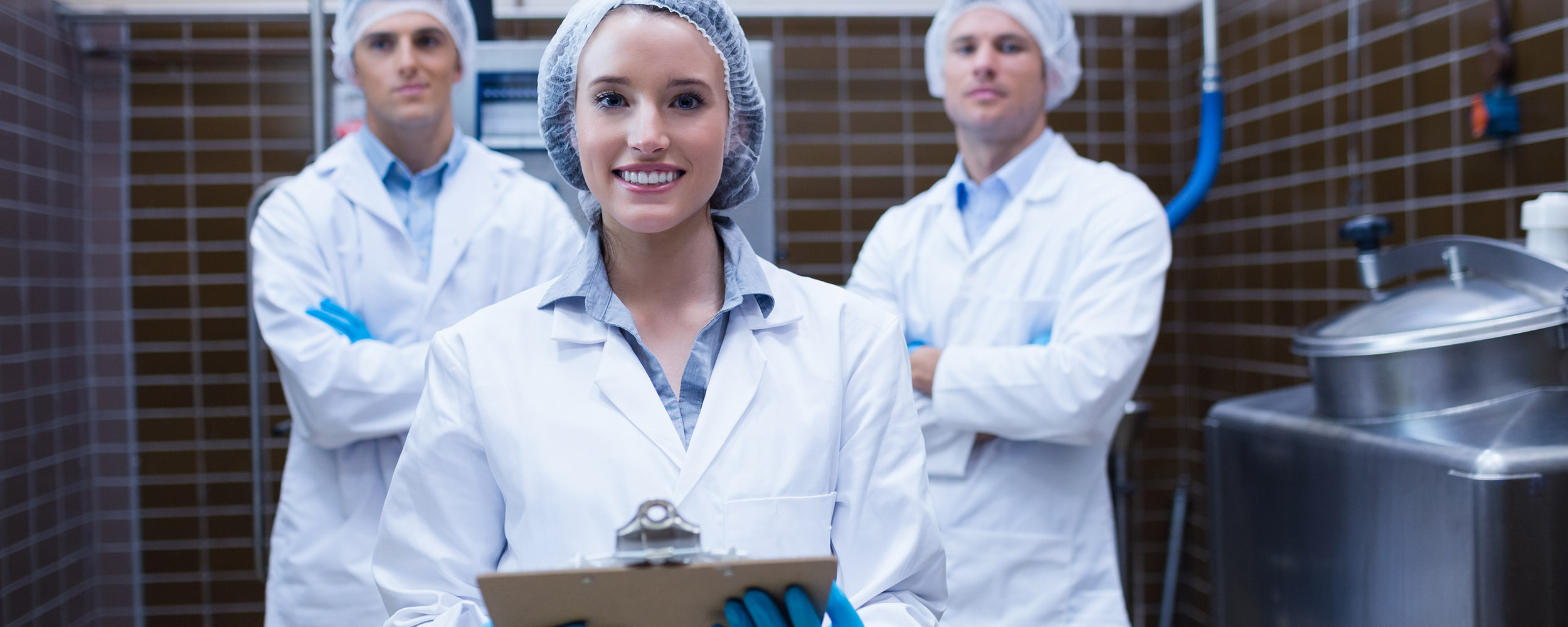 Girl holding a clipboard with these colleagues behind her in the factory